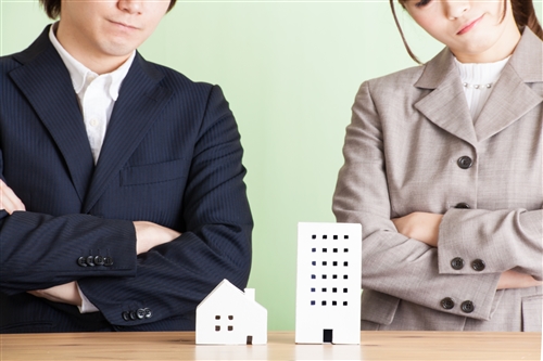 一戸建てとマンションの模型を並べて、男女が悩んでいる